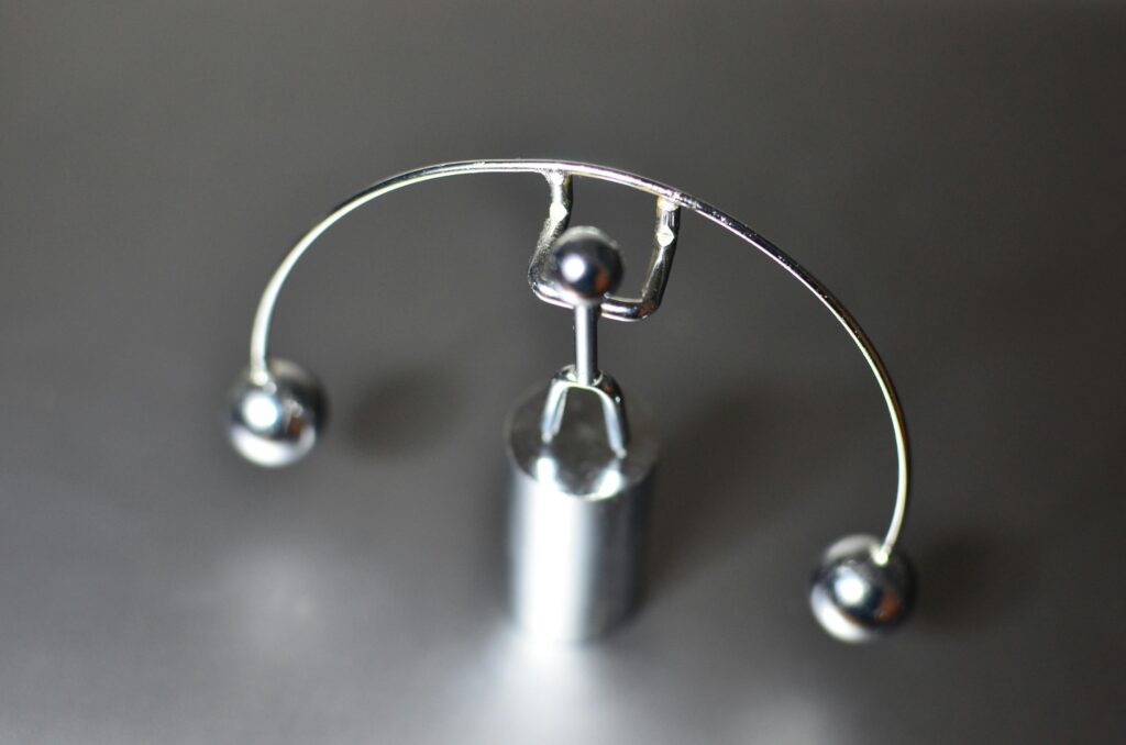 Stainless weightlifter kinetic perpetual dynamic motion toy with balance balls placed on gray table in light room on blurred background