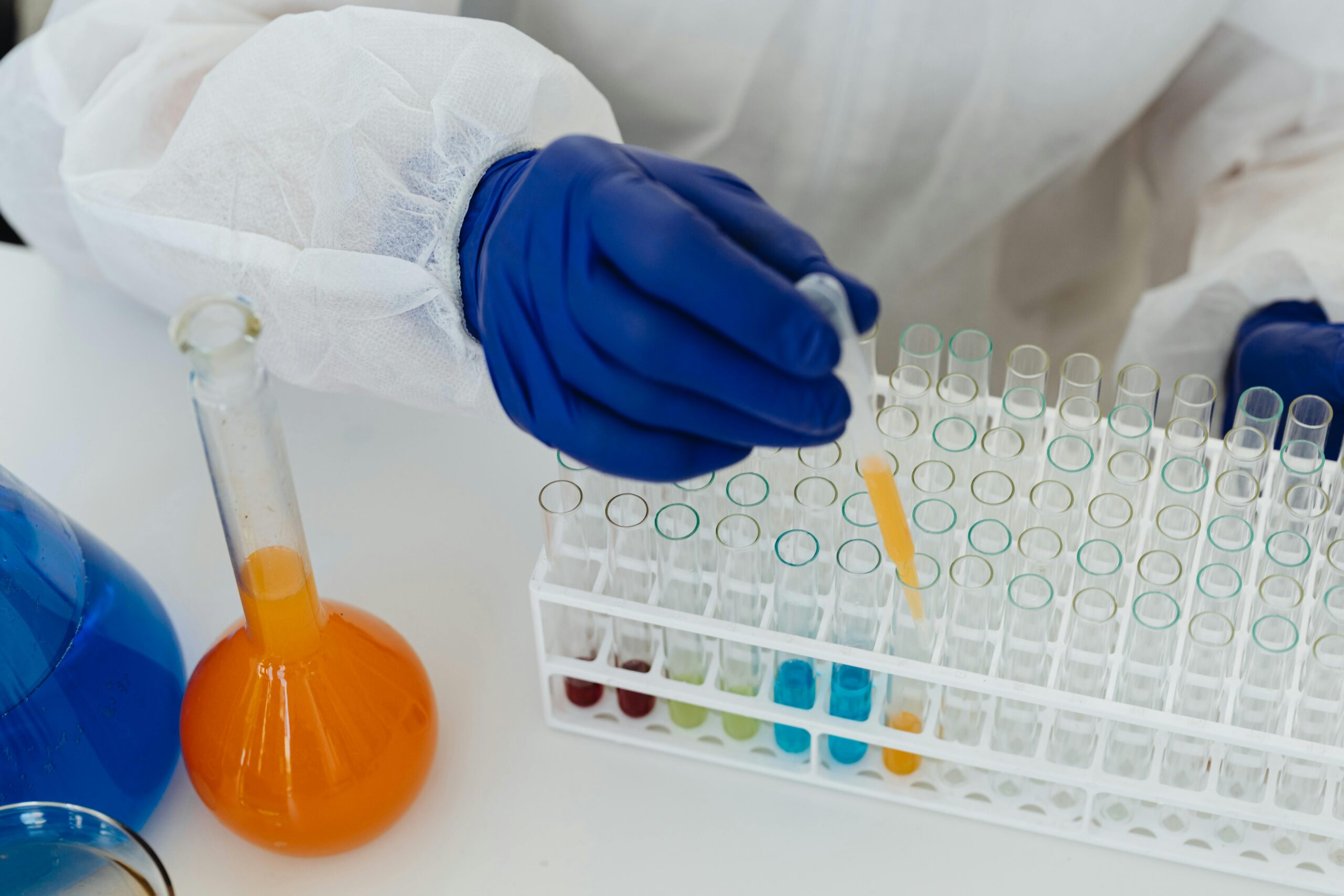 A scientist in blue gloves uses a pipette to handle colored liquids in a laboratory setting.